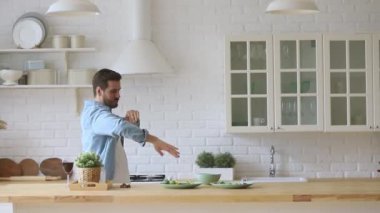 Komik aktif genç adam evde tek başına dans edip yemek yapıyor.