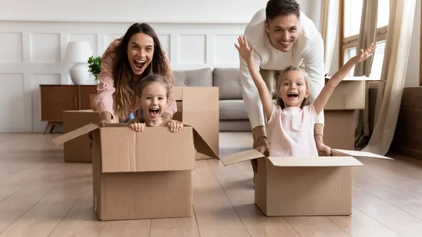 Excited family having fun on moving day riding in boxes — Stock Photo, Image