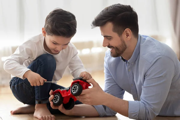 Отец помогает маленькому сыну ремонтировать игрушечный красный грузовик. — стоковое фото