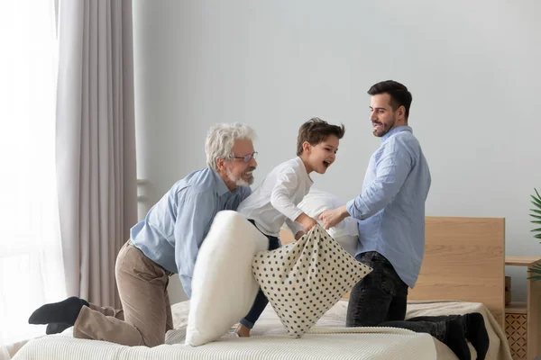 Tres generaciones de hombres juegan con almohadas en la cama adentro —  Fotos de Stock