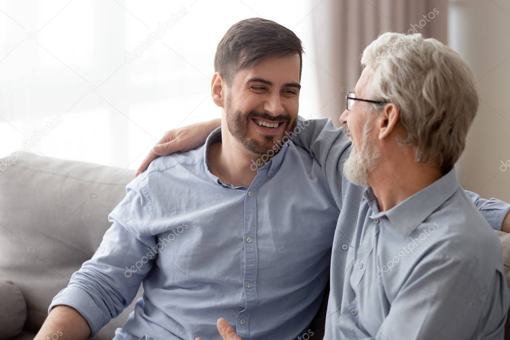 Aged father grownup son laughing having fun sitting on couch
