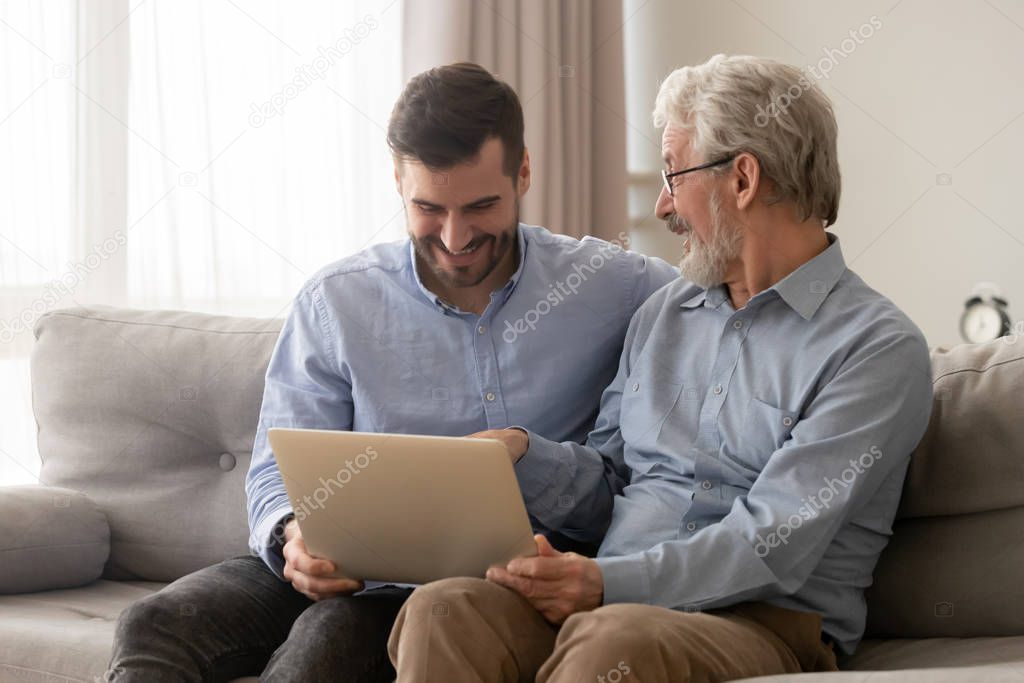 Father and grown up son sit together on couch with laptop