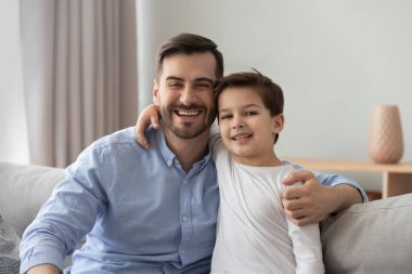 Baba oğlunu kucaklıyor kanepeye oturmuş kameraya bakıyor.