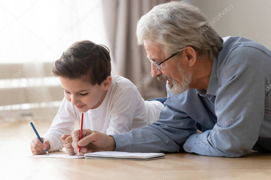 Grandfather drawing with grandson using colored pencils lying on floor