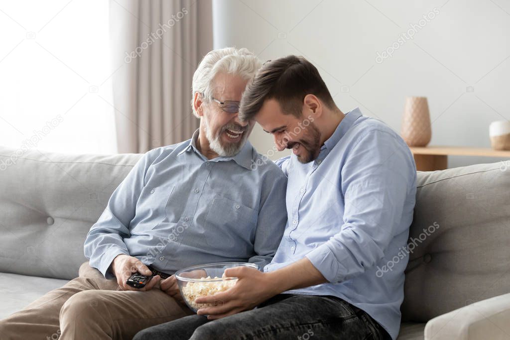 Elderly father grownup son laughing eating popcorn enjoy weekends together