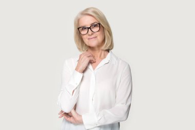 Gözlüklü, gülümseyen yaşlı kadın stüdyoda poz vermekten utanıyor.