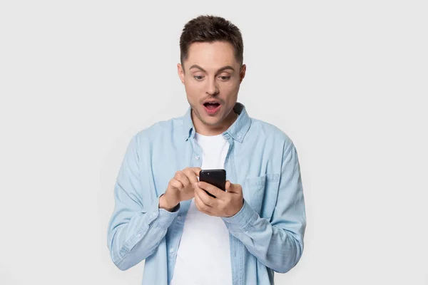 Překvapený tisíciletý muž držící mobilní telefon při pohledu na obrazovku telefonu — Stock fotografie
