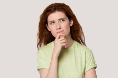 Kuşkulu, kızıl saçlı genç bir kadın çenesine dokunuyor, yukarı bakıyor..