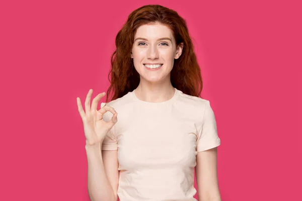 Happy millennial red-haired woman looking at camera, showing ok gesture. — Stockfoto