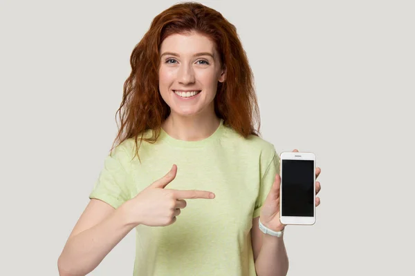 Spännande ung rödhårig kvinna demonstrerar ny modell mobiltelefon. — Stockfoto
