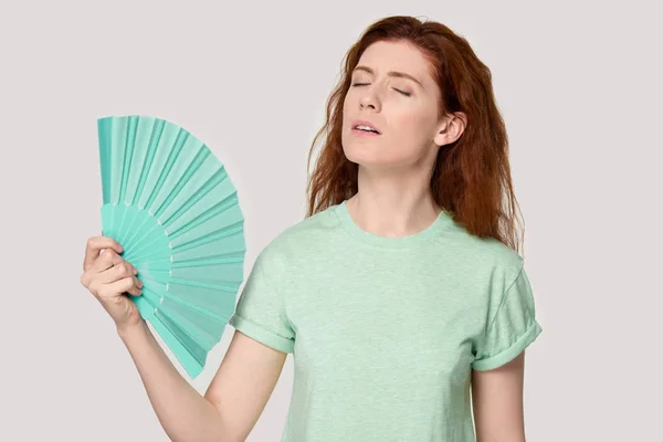 Überhitzte junge rothaarige Frau kühlt sich mit Ventilator ab. — Stockfoto