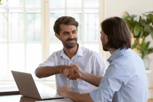 Sorrindo jovem empresário apertando as mãos com confiante colega de trabalho masculino . — Fotografia de Stock