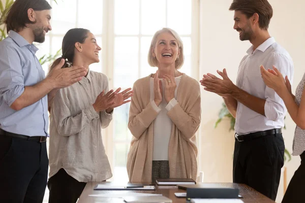 Happy middle aged team leader surprised by diverse colleagues congratulations.