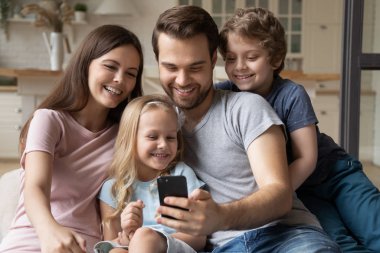 Akıllı telefon kullanan çocuklu bir aile evde eğleniyor.