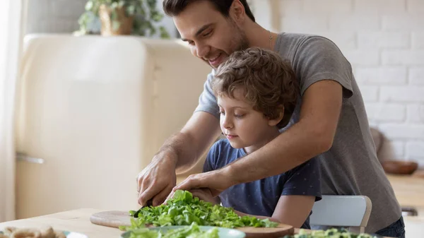 In domestic kitchen father teaches little son how cook salad