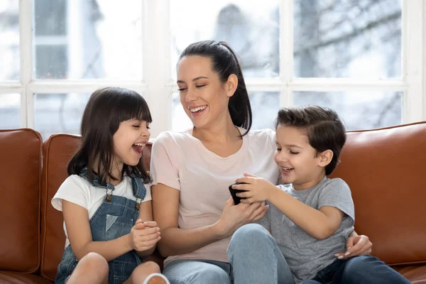 Lycklig mor med skrattar söt dotter och son med hjälp av smartphone. — Stockfoto