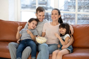 Mutlu genç aile ve anaokulu çocukları komik TV dizileri izliyor.