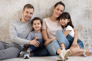 Gri arka planda iki çocuklu mutlu aile portresi.
