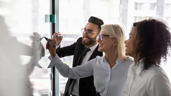 Smiling diverse colleagues brainstorm writing on whiteboard — Stock Photo, Image