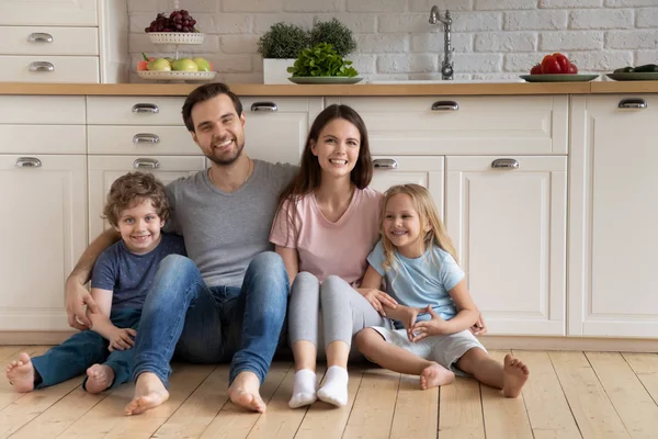 キッチンの暖かい床に座って抱きつく子供たちと家族 — ストック写真