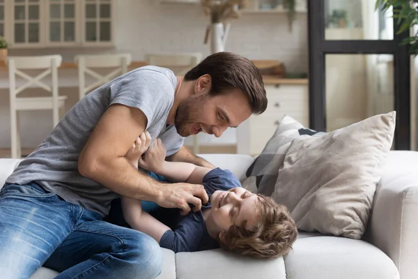 Vater kitzelt liebenswerten Sohn, der Spaß im Wohnzimmer hat — Stockfoto