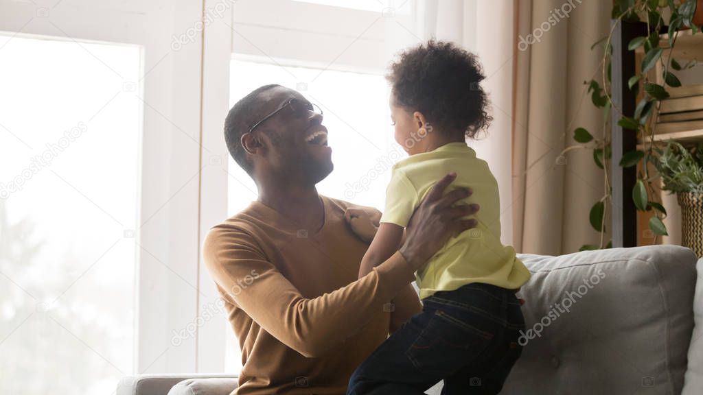 Happy black dad and son have fun playing on couch