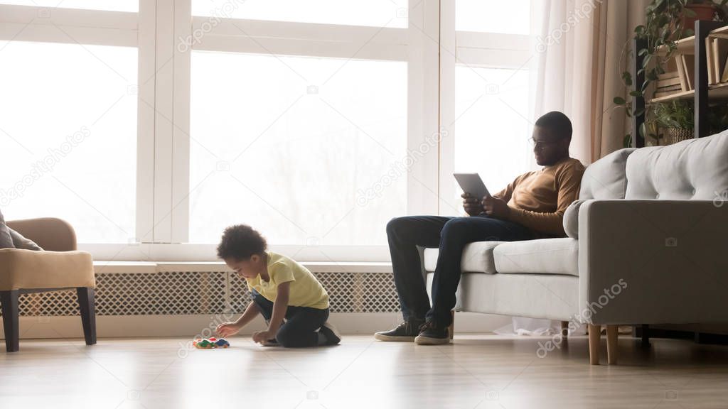 Black father use laptop little son play cars at home
