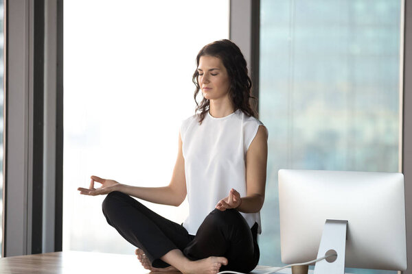 Peaceful businesswoman meditating on desk in modern office