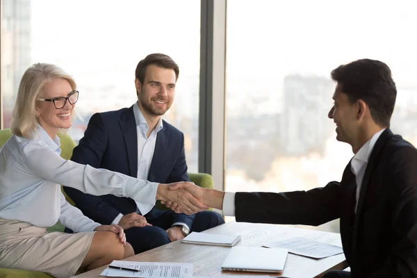 Smiling mature businesswoman shaking hand of business partner at meeting — Stock Photo, Image