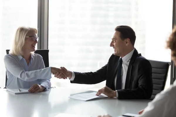 Excited mature businesswoman shaking hand of business partner at meeting — Stock Photo, Image