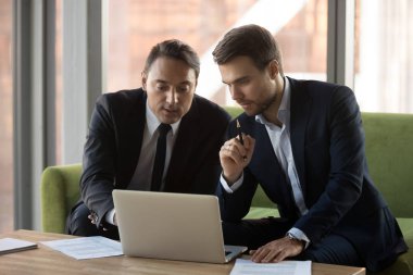 Ciddi iş adamları birlikte çalışıyor, dizüstü bilgisayar kullanıyor, projeyi tartışıyorlar.