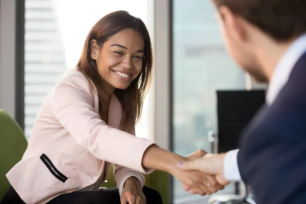 Smiling African American businesswoman shaking hand of businessman