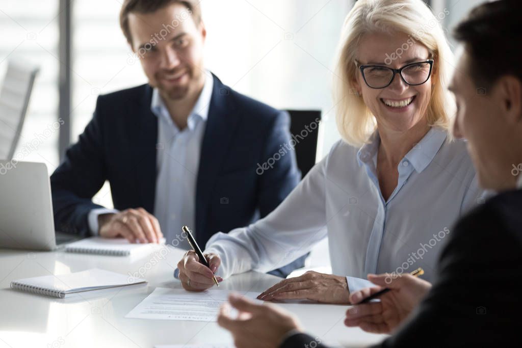 Smiling mature businesswoman signing contract, agreement at meeting