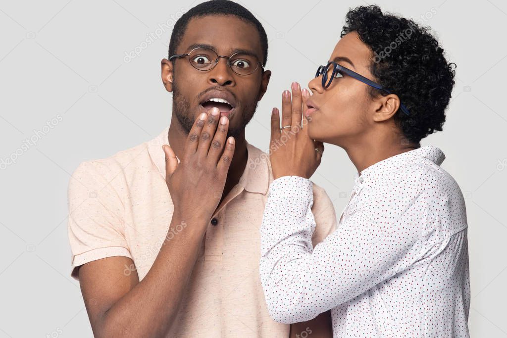 Young african american woman in eyeglasses whispering secret to husband.