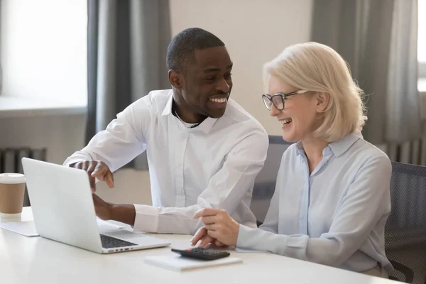 Smiling diverse workers laugh working on laptop together — Stock Photo, Image