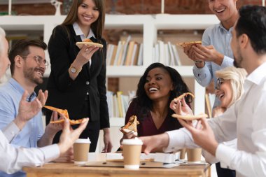 Farklı etnik kökenli meslektaşlar iş saatlerinde öğle yemeği sırasında pizza yerler.