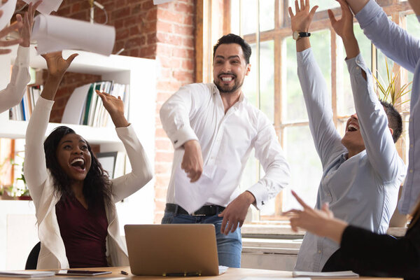 Excited team celebrating successful project accomplishment throwing papers up