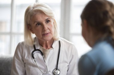 Orta yaşlı kadın doktor konuşması küçük bir hastayı muayene ediyor.
