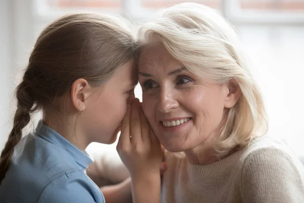 Little girl whisper in ear tell secret to curious grandmother — Stock Photo, Image
