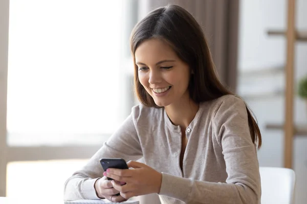 Chica feliz sentarse en la mesa leer mensaje agradable en el teléfono inteligente —  Fotos de Stock