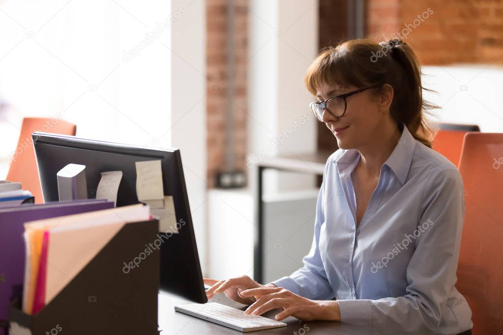 Middle aged employee typing using keyboard looking at computer screen