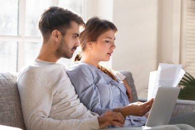 Odaklanmış genç çift faturaları kontrol ediyor, dizüstü bilgisayarlı kredi belgeleri birlikte.