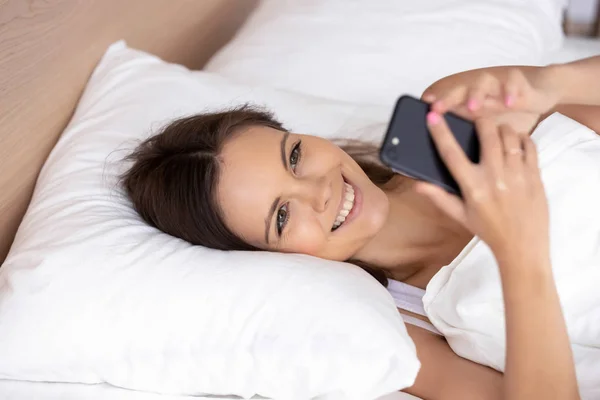 Smiling girl wake up checking cellphone in morning