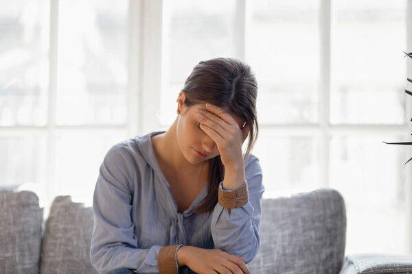 Upset young woman hiding face, crying, thinking about problem