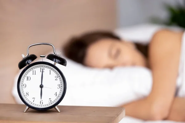 Alarm clock on bedside table with woman sleeping on background Stock Picture