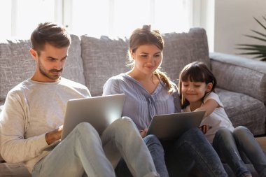 Küçük kızı olan bir aile yerde oturuyor, birlikte dizüstü bilgisayar kullanıyorlar.