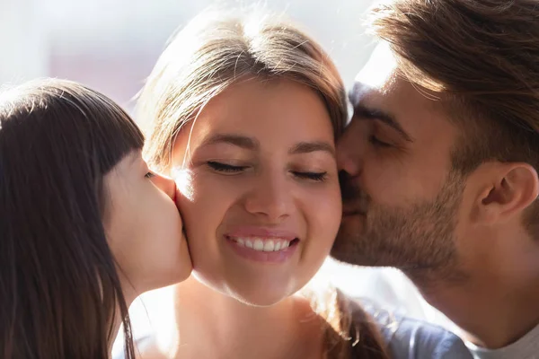 Маленькая дочь и отец целуют улыбающуюся мать жену в щеки — стоковое фото