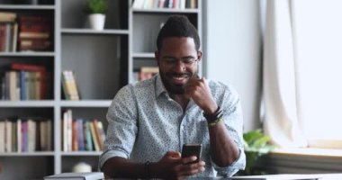 Ofiste akıllı telefon kullanan mutlu, genç Afrikalı adam.