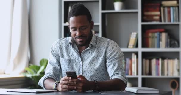 Akıllı telefon kullanan genç bir Afrikalı ofis masasında oturuyor. — Stok video