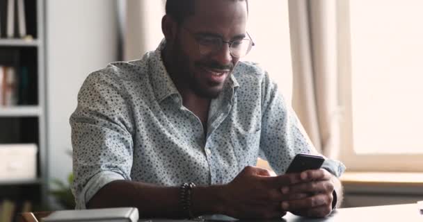 若いですアフリカの男を笑顔モバイルアプリを使用して座ってテーブル — ストック動画